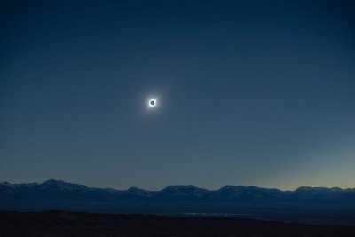 Image of the total solar eclipse with the solar corona in the sky above a mountain range in the distance.