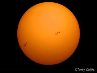 The photo shows the Sun as an orange disc with two groups of dark areas on its surface which are the sunspots.